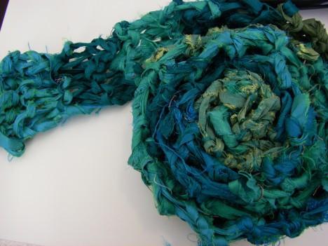 Teal knitted scarf rolled up onto a white surface