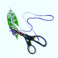 Finished woven leave with purple and white yarn with excess getting cut by scissors.