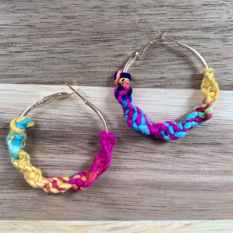 Finished multi-colored yarn earrings on wood background.