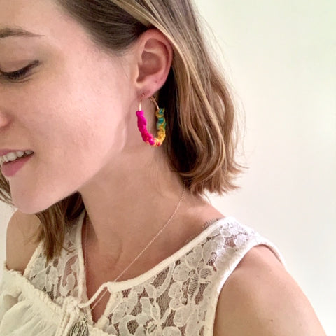 Close up of finished macrame earrings on young woman wearing white dress with blonde hair