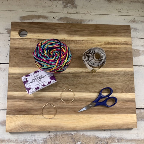Gathered materials for DIY earrings on a wood craft board: Darn Good Yarn Silk Roving Worsted Weight Yarn, Hoop earrings (size ½” or larger is ideal, tutorial is created using 1”), measuring tape and scissors