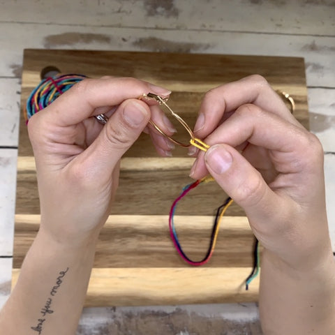 Hands threading yarn onto one earring hoop
