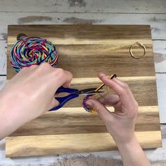 Hands and scissors cutting excess yarn off of knot
