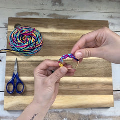 Hands gently twisting multicolored yarn on earring hoops