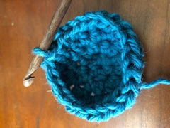 Showing the cup of the cactus begin to form with teal yarn and wooden crochet hook
