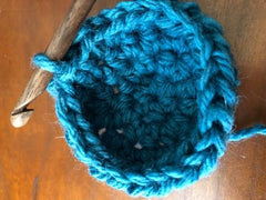 Wooden crochet hook and teal yarn showing cactus cup begin to form.