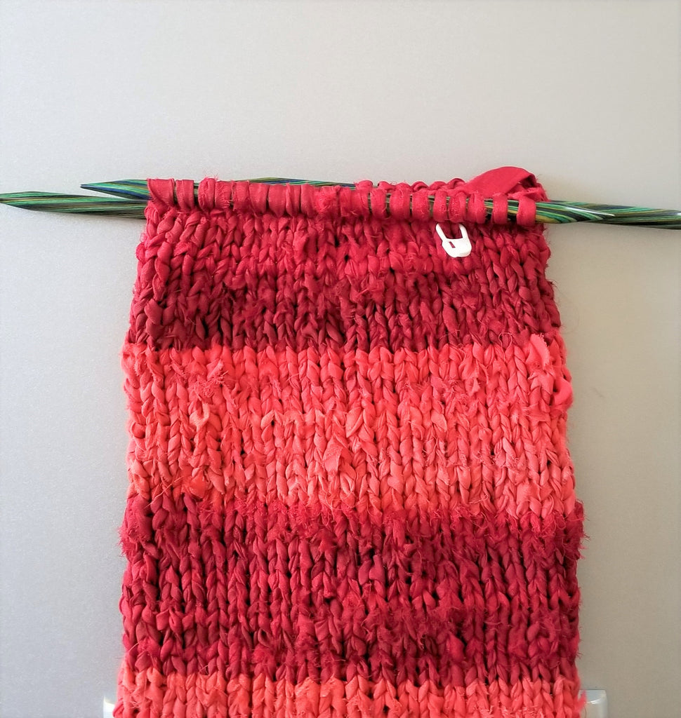 Red striped knit stocking with knitting needles on a white background