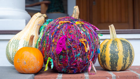 Yarn-wrapped pumpkin with three other gourds sitting on a front porch step