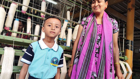 An artisan smiles in pride at her son, who is wearing a bright blue school uniform.