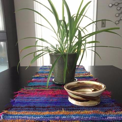 Tibet Jewels Woven Table Runner on a black tabletop with a wooden bowl and large potted houseplant in front of a large window