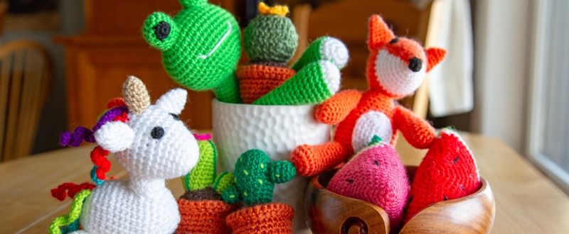 A frog, fox, unicorn, cacti, and watermelon amigurumi sitting in a yarn bowl.