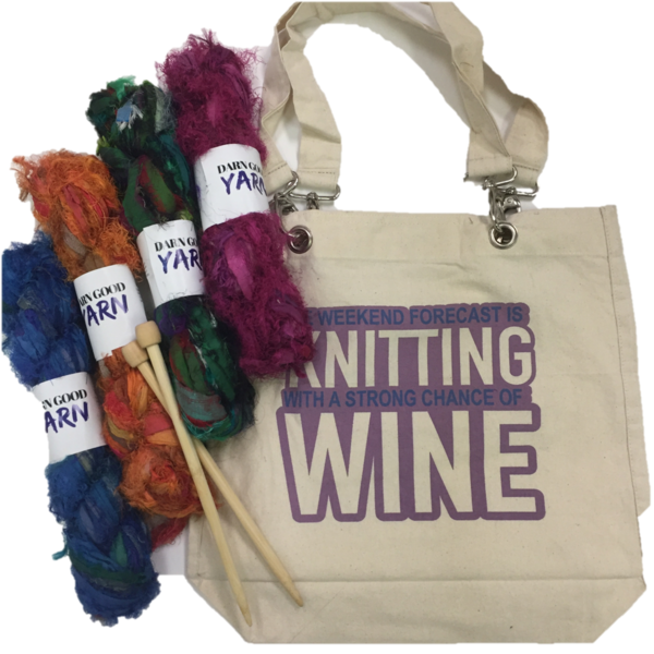 Beige tote bag with purple text that reads 'Weekend forecast is knitting with a strong chance of wine', 4 skeins of silk yarn in blue, orange, green, and purple, and wooden knitting needles all on a white background