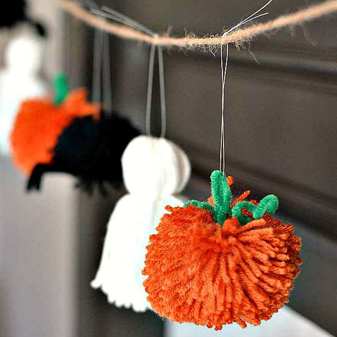 Pumpkin, ghost, and spider yarn garland hanging in front of a black wall