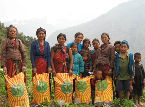 Multiple Women and children holding large yellow bags and standing amongst greenery