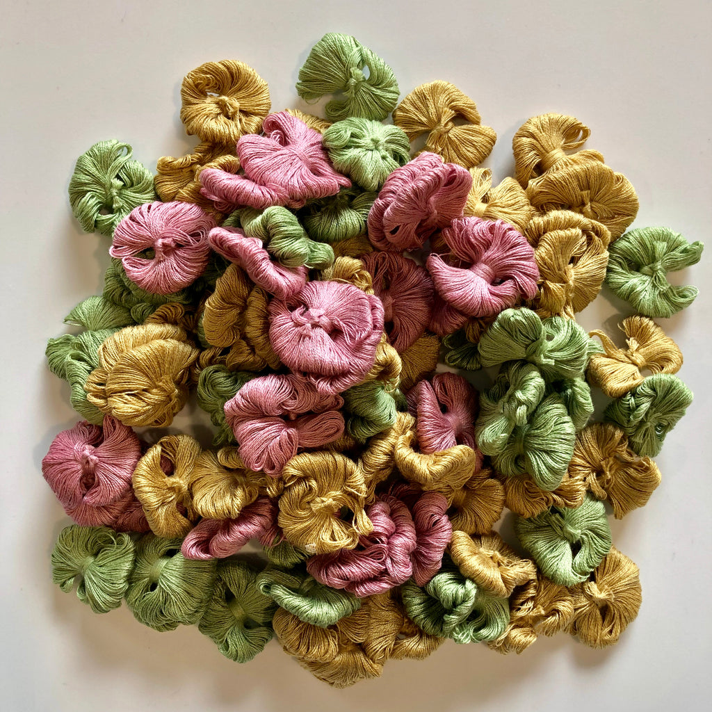 Pile of pink, green, and yellow cotton thread samples on a white background