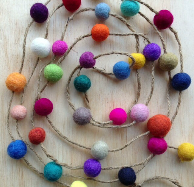 Multicolored felt balls strung on a long strand of hemp yarn, all laid on a wooden surface