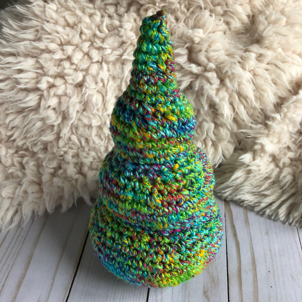 Blue and green crochet Christmas Tree sitting on a wooden surface next to a white fur blanket