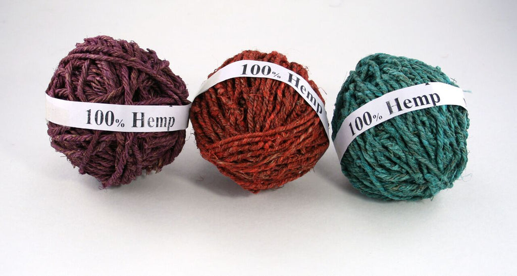 3 balls of hemp yarn in purple, rust, and teal sitting on a white background