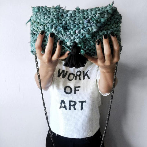 Woman's hands holding a turquoise Tasseled Sari Silk Clutch in front of a white tee shirt that reads 'Work of Art' and standing in front of a white wall