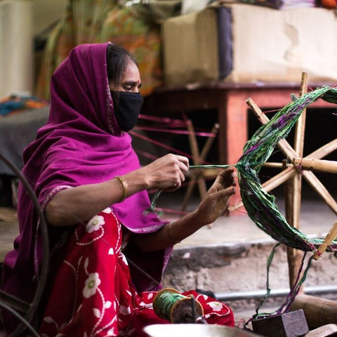 green Sari Silk Ribbon being spun on a swift by a woman sitting on the ground wearing a pink and red sari