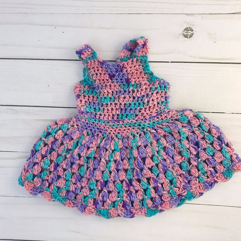Pink, blue, and purple crochet sundress for a doll laid on a white wooden background