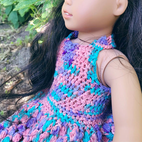 Close up of an 18" doll with dark hair wearing a pink, blue, and purple crochet sundress