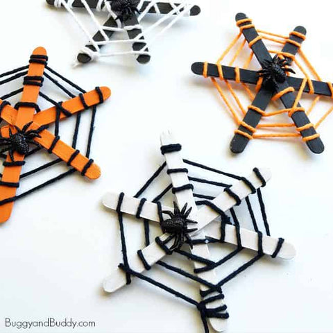 3 Popsicle stick and yarn spider webs with plastic spiders sitting on a white surface