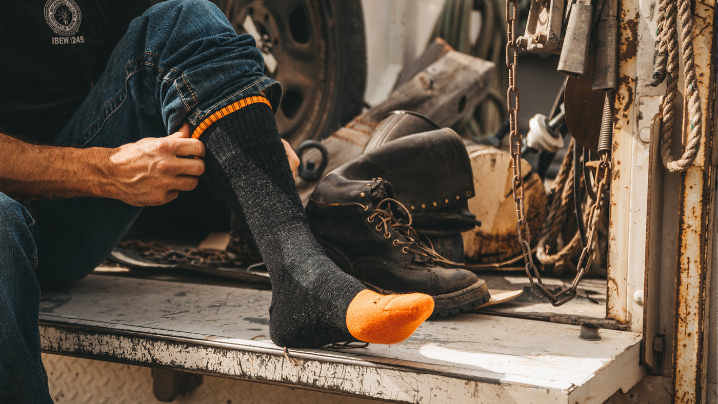 Worker pulling on leather steel toe boots over darn tough work socks with steel toe cushion