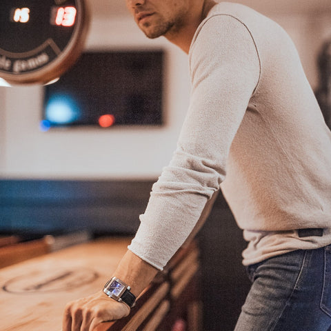 Fyrkantig klocka i borstat stål med romersk & blå urtavla - Fyrkantig klocka på man som spelar shuffle board