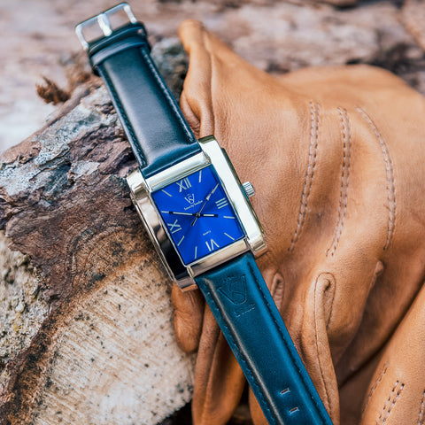 Herrklocka i polerat stål med blå klassisk urtavla - närbild på klockan på en stumme tillsammans med skinnhandskar