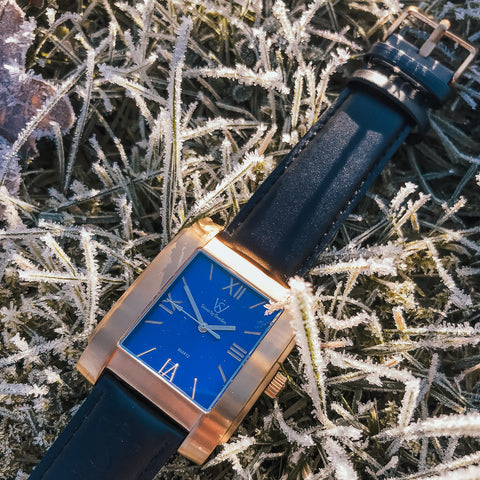 Fyrkantig herrklocka i borstat guld med blå romersk urtavla liggandes i i frostigt gräs på vintern