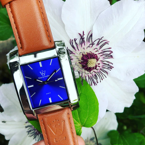 Fyrkantig herrklocka i polerat stål med blå klassisk urtavla - Närbild på fyrkantig klocka med en blomma i bakgrunden