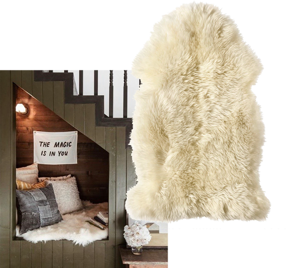 a cozy snug has been built into a staircase. Throw pillows, a pile of books and a sheepskin rug add warmth to this compact cubby hole. A small fabric sign reads "the magic is in you"