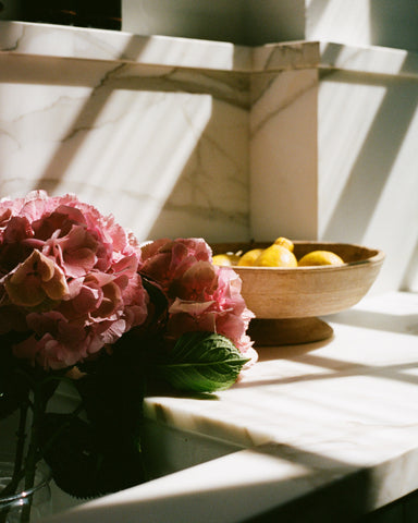 some fresh pink flowers next to a wooden bowl of lemons