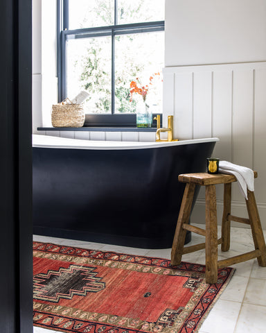 a beautiful black bathtub with an antique wooden stool and rug beside it