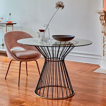 a round metal table with a pink chair beside it and a single flower in a vase