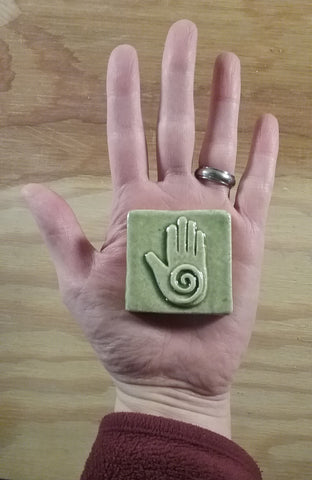 light green two inch by two inch healing hand handmade tile in the palm of a hand