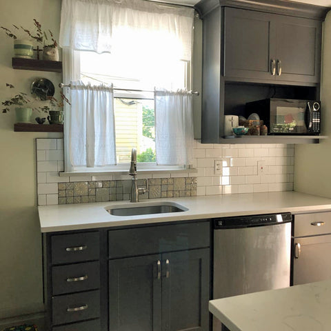 A newly remodeled kitchen with gray cupboards, white counters and subway tiles, and a handmade tile feature over the sink