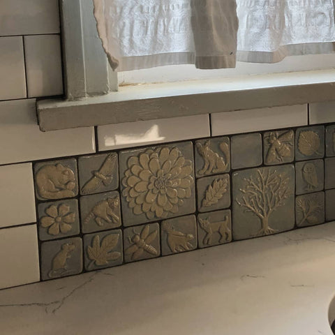 close up of handmade tiles in a light purple glaze featuring plants and animals, installed with with subway tiles in a newly remolded  kitchen