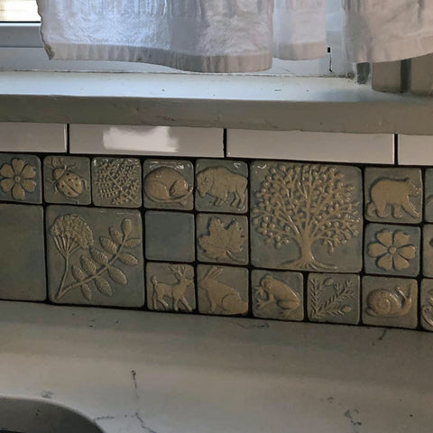 close up of handmade tiles featuring plants and animals installed in a kitchen backslash 