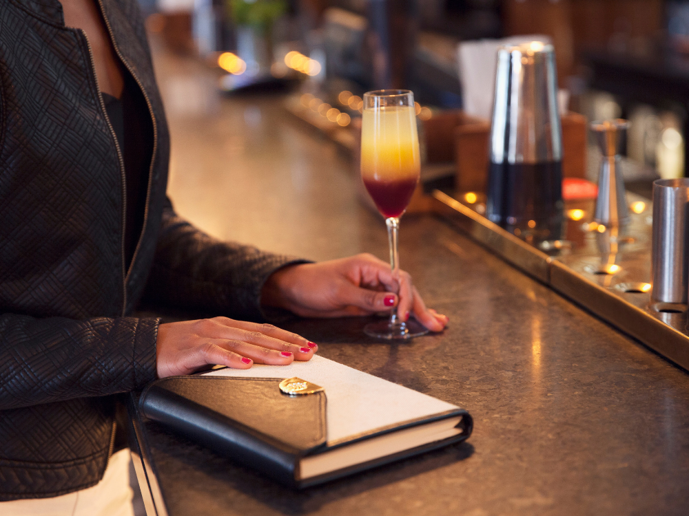 woman stood at a bar with a notebook and cocktail