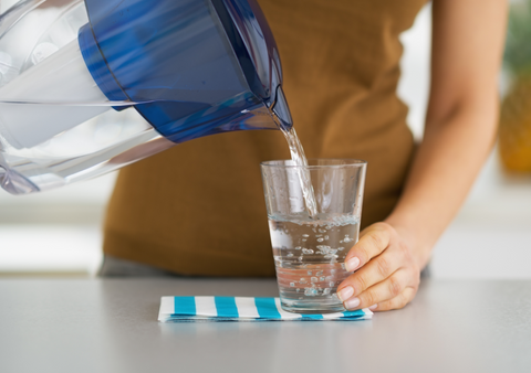 woman pouring water into glass from water filter pitcher