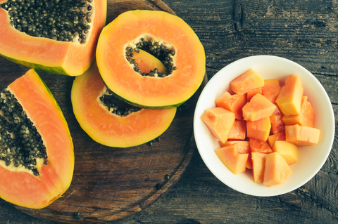 Slices of ripe sweet papaya in white bowl on old wooden background