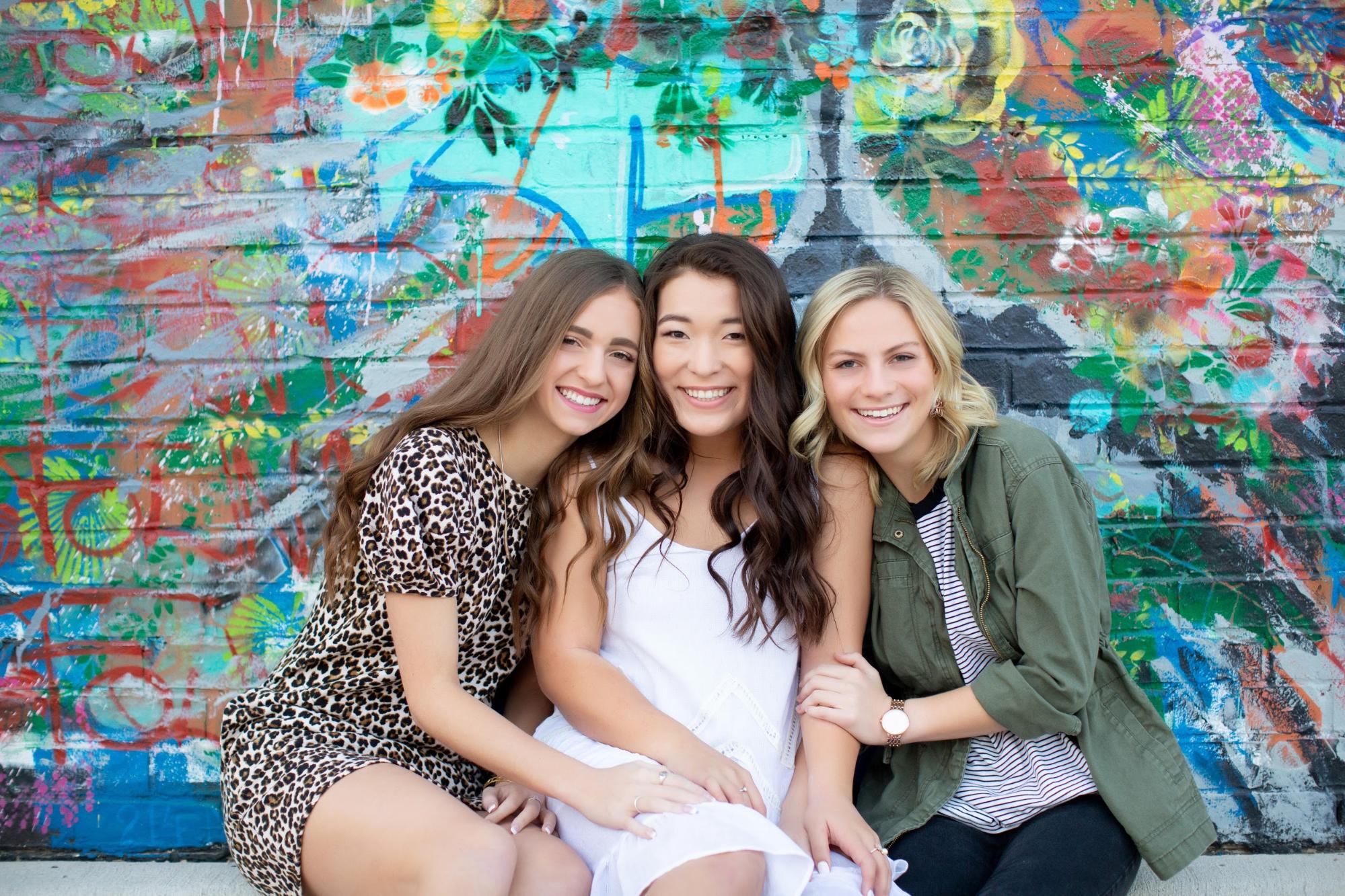 Three girls leaning up close to each other with mural background