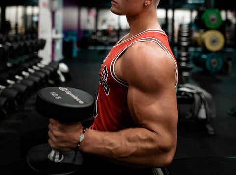 Bodybuiler in an orange jersey top carrying a dumbbell