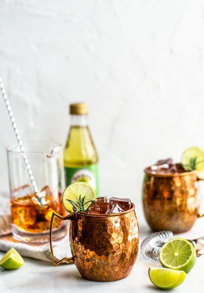 two Moscow Muled copper mugs filled with ice cubes and herb sprig