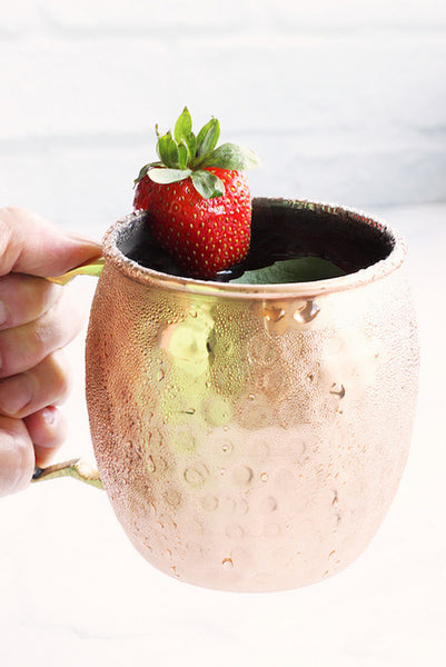 hand holding Moscow Muled mug filled liquid and strawberry wedged on its rim