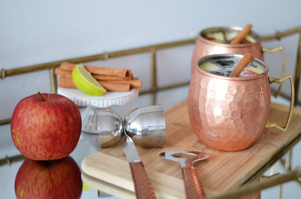 two Moscow Muled copper mugs filled with liquid apple slices and cinnamon sticks