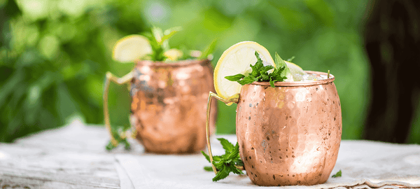 two Moscow Muled copper mugs filled with ice lemon mint leaves and lemon slice