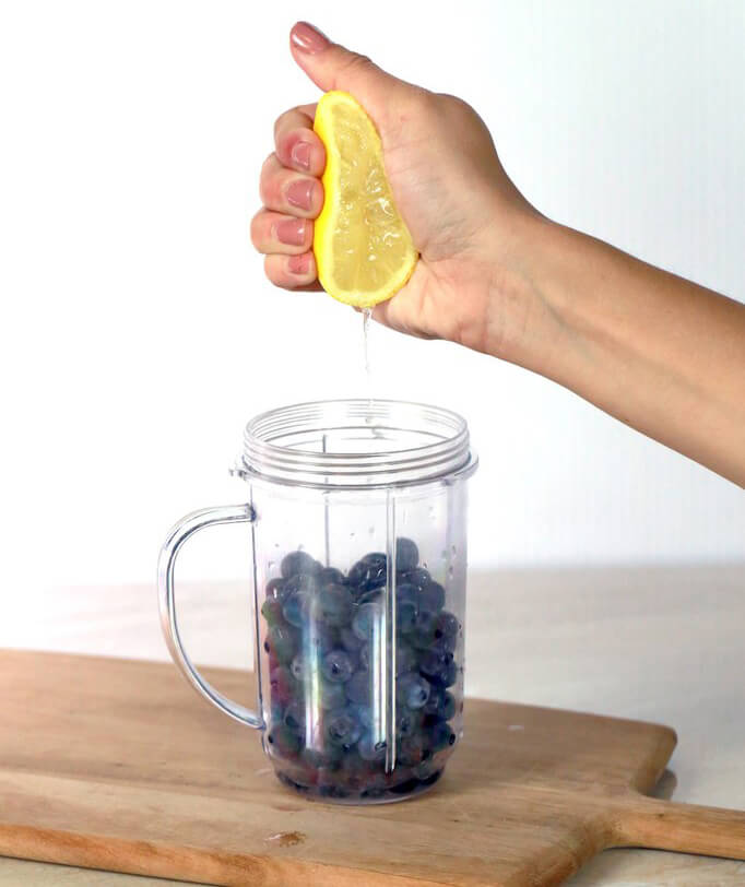 hand squeezing lemon into a clear blender jar of blueberries